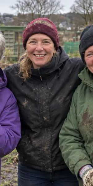 Three gardeners with spades, smiling among the vegetable beds of an allotment